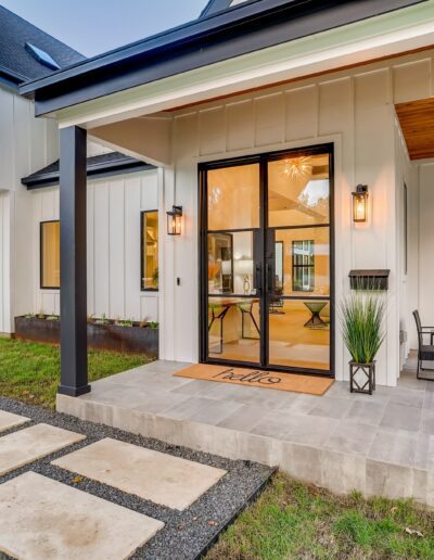 Modern house entrance with a concrete pathway, a "hello" doormat, and outdoor seating.