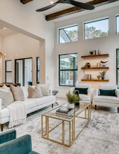 Modern living room with high ceilings, large windows, and a mix of white and teal furniture.