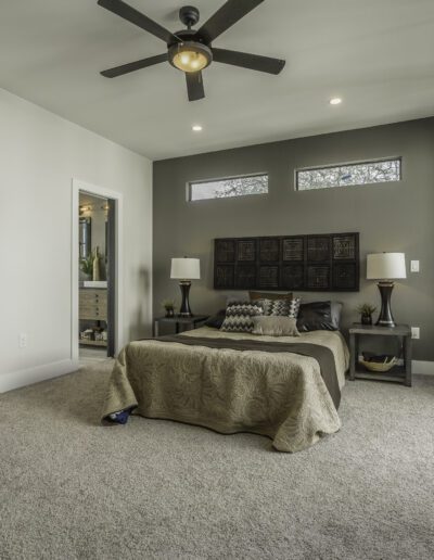A modern bedroom with neutral tones, large windows, and a ceiling fan.