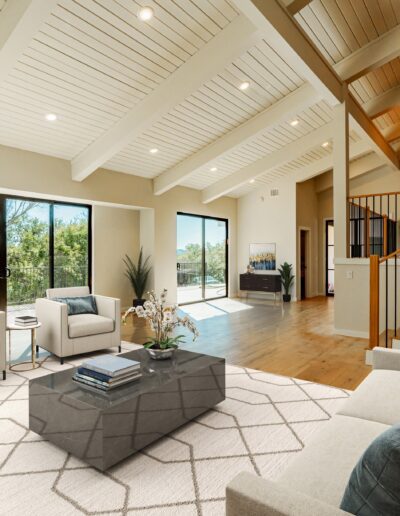Spacious living room with high vaulted ceiling, large windows, and a modern staircase.