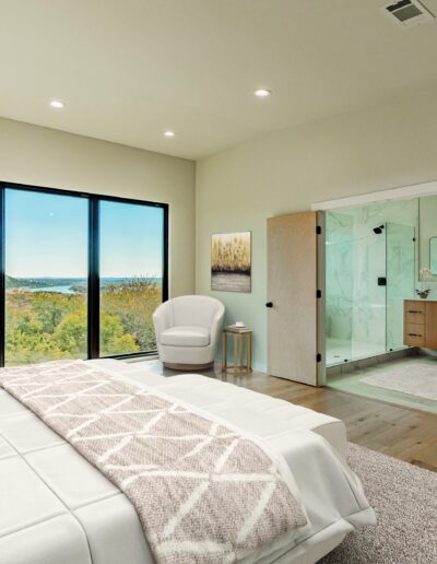 A modern bedroom with floor-to-ceiling windows offering a scenic view, featuring a large bed, an armchair, and an en suite bathroom.