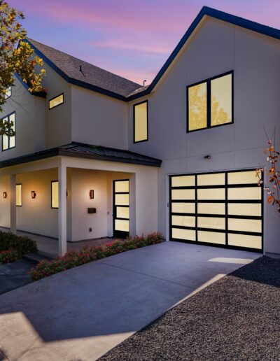 Modern two-story house at dusk with illuminated windows and an attached garage.