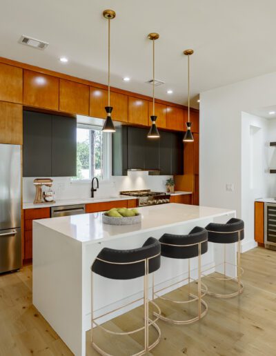Modern kitchen with wooden cabinets, stainless steel appliances, and a white island with black stools.