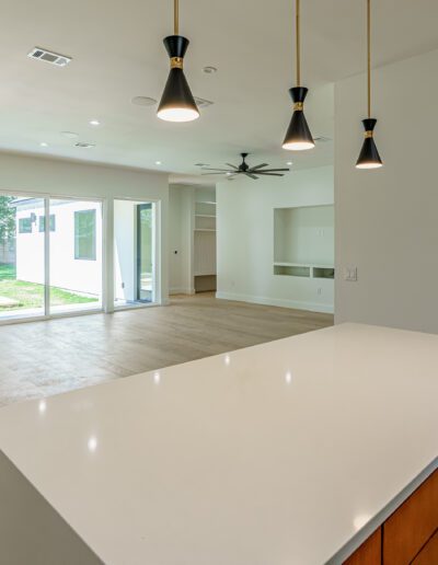 Modern, spacious kitchen with white countertop island, pendant lights, and an open-plan living area with a view of the yard.