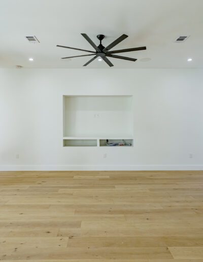 Empty modern living room with hardwood floors, white walls, recessed shelving, and a black ceiling fan.