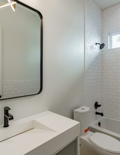 A modern bathroom with white subway tiles, a bathtub, and a vanity with a black-framed mirror.