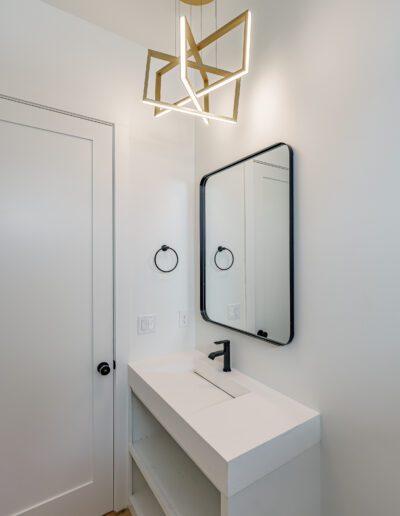 Modern bathroom interior with geometric light fixture, rectangular mirror, and white vanity.