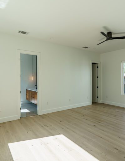Bright, empty room with hardwood floors, ceiling fan, and windows with a view into a neighboring room.