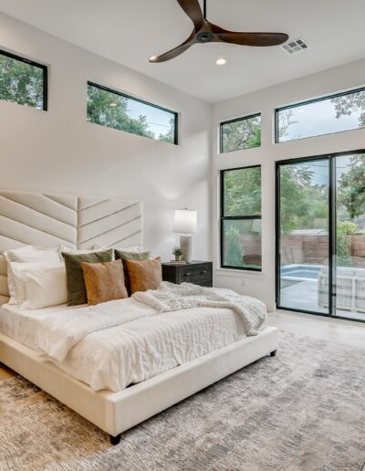 Modern bedroom with large windows, a ceiling fan, and direct access to the patio.