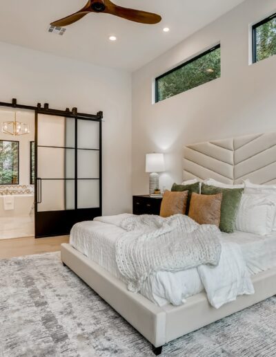Modern bedroom interior with neutral colors, a tufted bed, and a combination of natural light and stylish lighting fixtures.