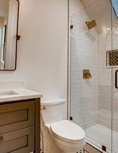Modern bathroom interior with white tiling, featuring a walk-in shower, toilet, and vanity with a mirror.