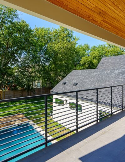 Spacious balcony with a metal railing, overlooking a pool and a tree-filled backyard on a sunny day.