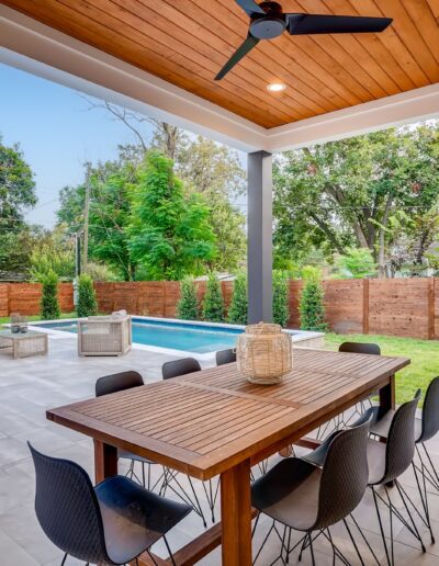 A modern outdoor patio area with dining set overlooking a swimming pool and landscaped garden.