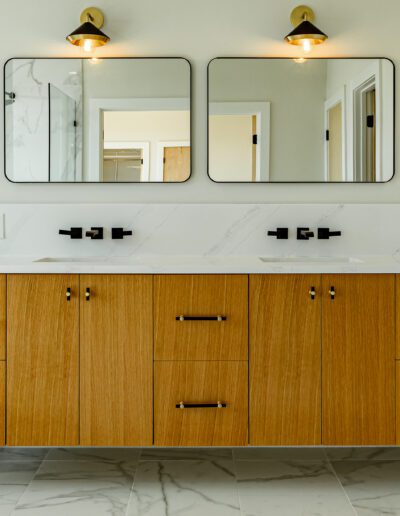 Modern bathroom vanity with dual sinks, wooden cabinetry, and wall-mounted mirrors flanked by sconce lighting.