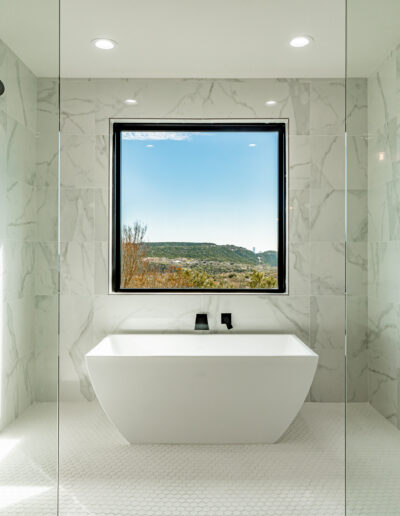 Modern bathroom with a freestanding bathtub, dual showerheads, and a large window with a scenic view.