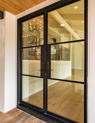 Modern home entrance featuring black french doors with large glass panes, leading into a brightly-lit interior with wooden floors.
