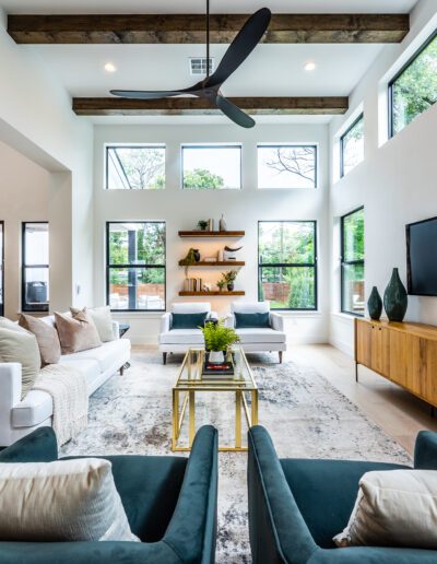 Modern living room with white walls, high ceiling with exposed beams, stylish furniture, and a large flat-screen tv on the wall.