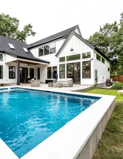 Modern two-story home with a backyard in-ground pool and patio area featuring lounge chairs.