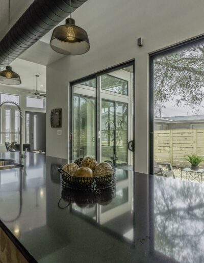Modern kitchen with black countertops, stainless steel appliances, and large windows overlooking a backyard patio.