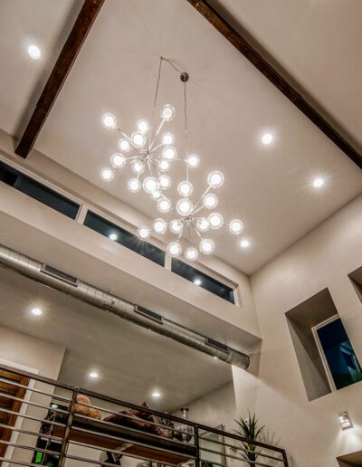 Modern interior of a room with high ceilings, featuring a large, spherical chandelier, exposed ductwork, and multiple windows.