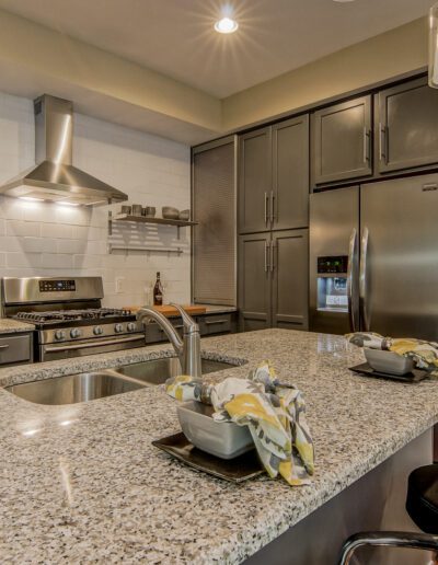 Modern kitchen interior with stainless steel appliances, granite countertops, and a breakfast bar with stools.