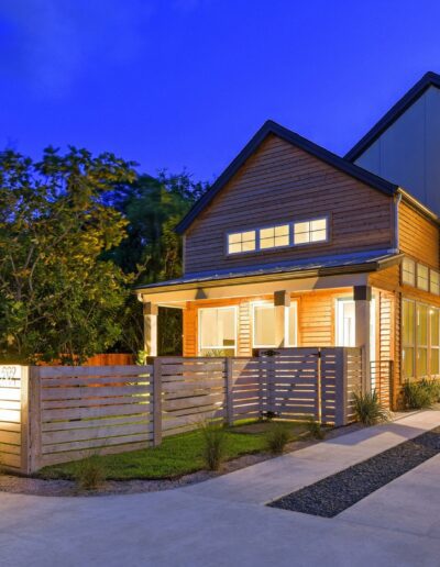 Modern two-story house illuminated at twilight with a landscaped walkway and wooden fence.