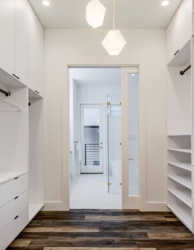 Modern walk-in closet with empty shelves and drawers, leading to a well-lit bathroom.
